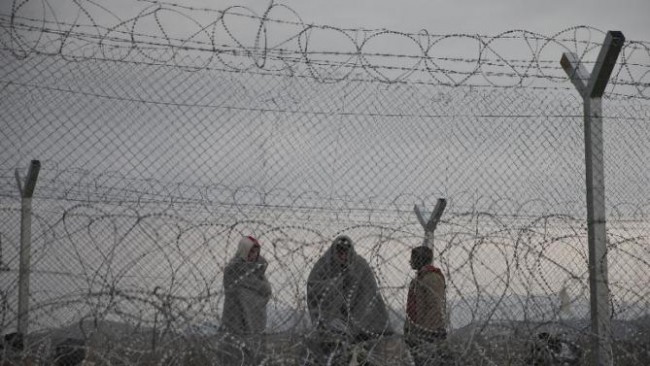 Migrants and refugees stand behind a fence reinforced with razor wire, on the border line with Greece near the southern Macedonia's town of Gevgelija, Monday, Feb. 29, 2016. More than 6000 migrants and refugees are stuck in the border after neighbor Macedonia began slowing the number of crossings heading to central and northern Europe. (AP Photo/Petros Giannakouris)
